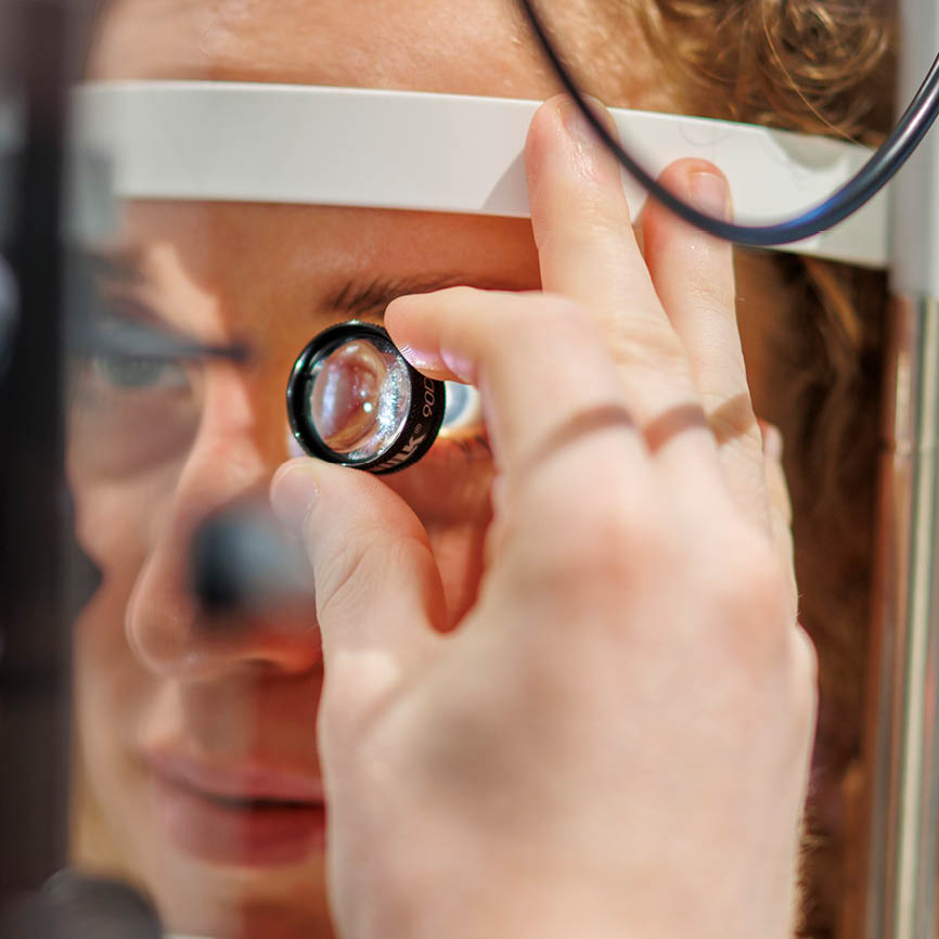 Optometrist kijkt naar de ogen van een vrouw en houdt een klein lensje tussen duim en wijsvinger voor haar oog